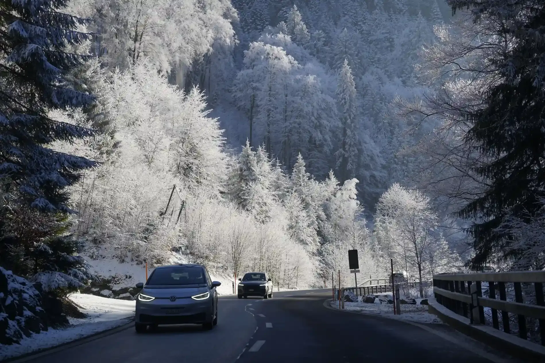 Auto elettrica con presa di ricarica coperta di brina parcheggiata in una mattina invernale con strada innevata