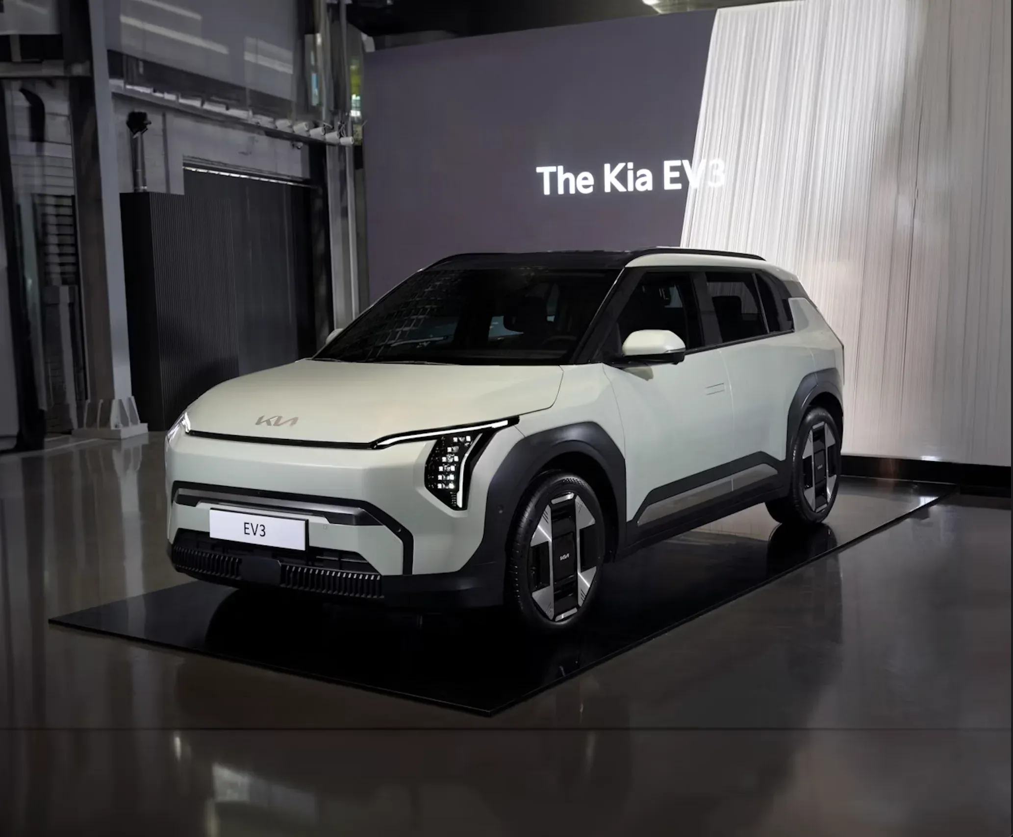 Kia EV3 grigia di tre quarti su strada extraurbana, frontale verticale con firma luminosa a LED e linee squadrate
