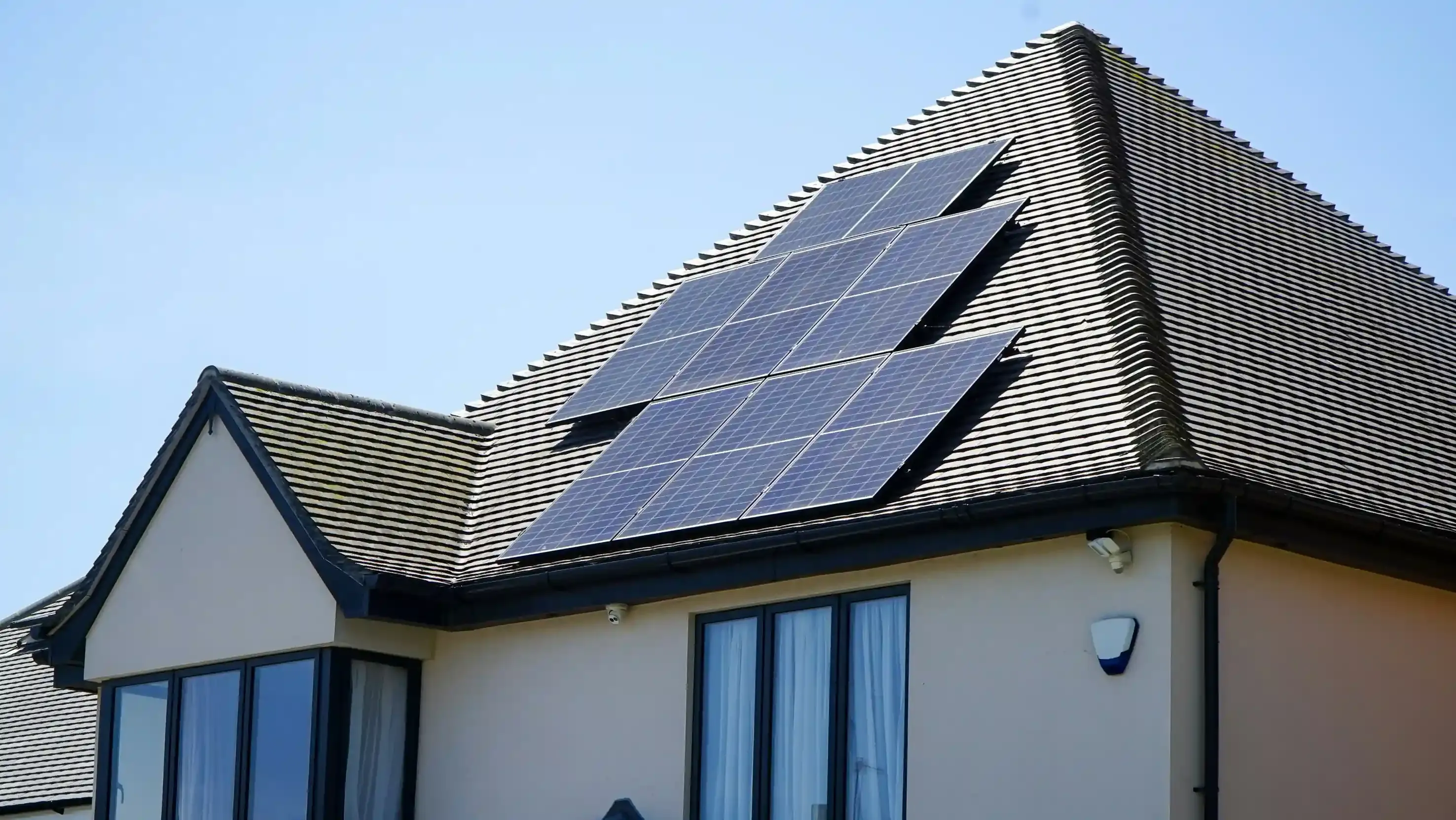 Auto elettrica collegata a una wallbox bidirezionale nel vialetto di casa con pannelli fotovoltaici sul tetto
